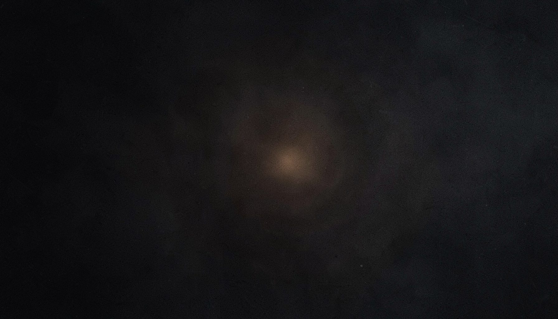 Abstract dark ambient texture with deep charcoal and muted slate tones, subtle grain, and a faint warm amber glow at the center suggesting electronic resonance.